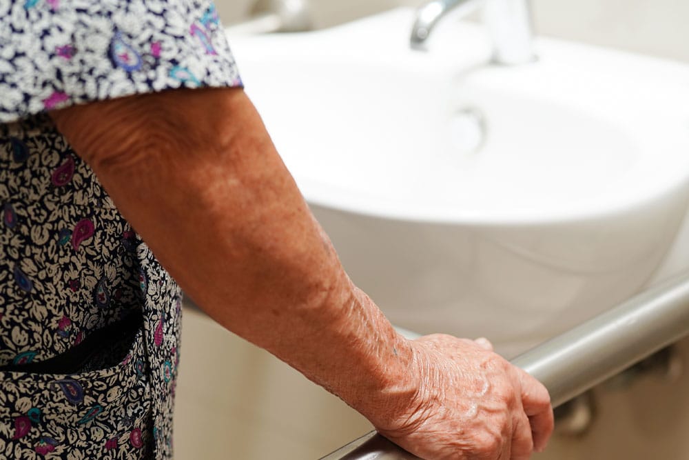 An aging woman gripping supports in a bathroom