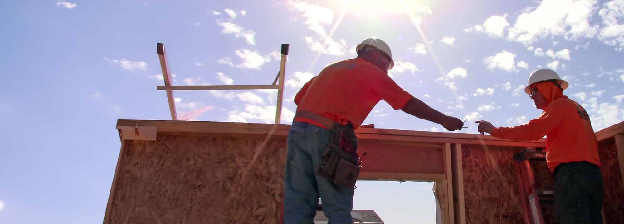 Two men with hard hats on working on the framing of a Habitat house