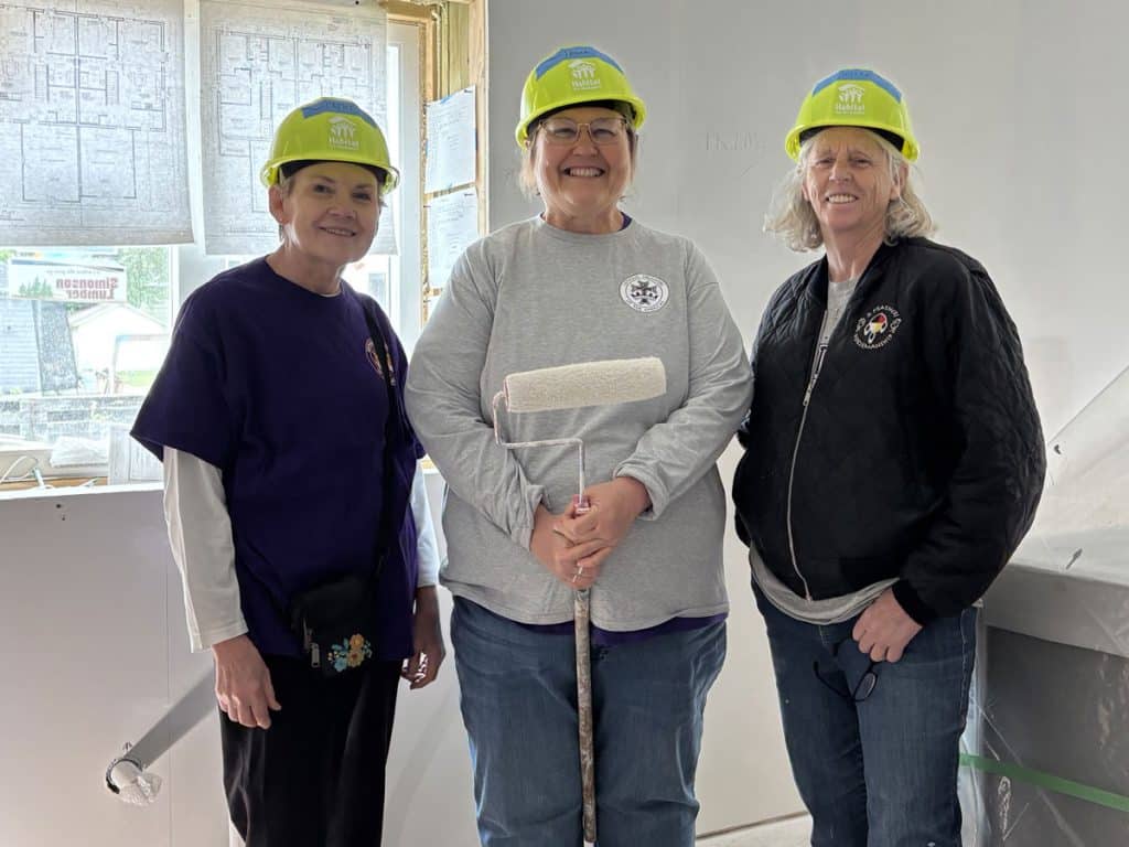 Three women volunteers inside a new build with Habitat hard hats on