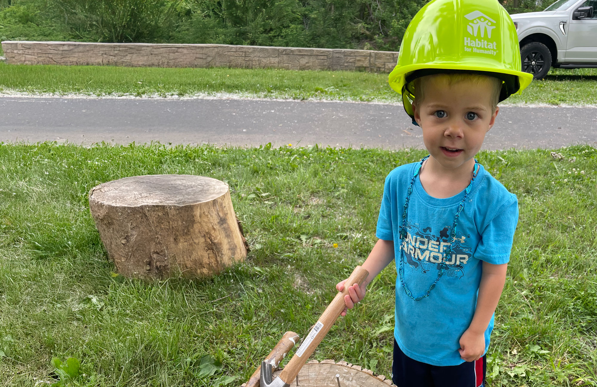 A young Habitat for Humanity volunteer holding a hammer and wearing a bright green hard hat
