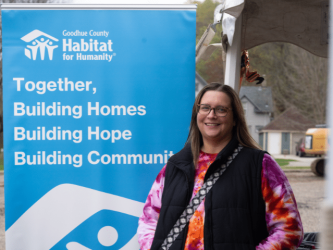 Habitat Homeowner standing in front of a op-up banner that reads 'Together, Building Homes, Building Hope, Building Community'