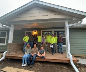 Volunteers, staff and family pose on the porch of a new Habitat build and dedication